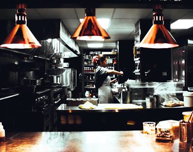 Image of a traditional servery window in a restaurant kitchen. Chef preparing food in background. Servery area with overhanging heat lamps in foreground.